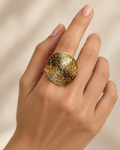 A close-up of a hand wearing a large round gold ring with a textured, crackled metallic surface.