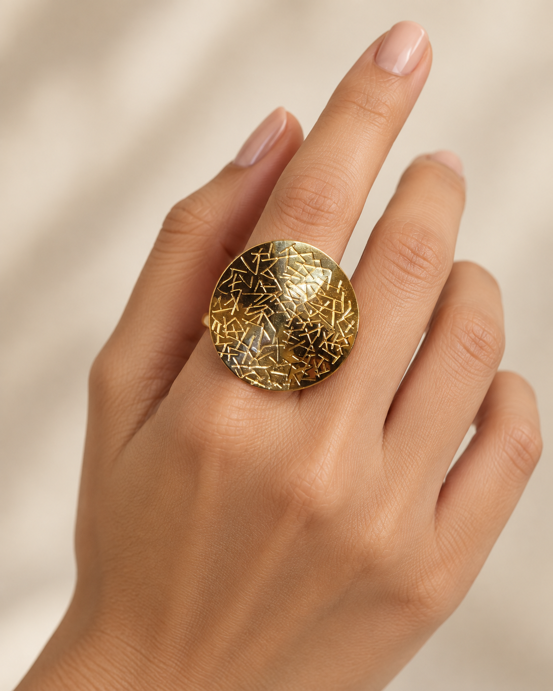 A close-up of a hand wearing a large round gold ring with a textured, crackled metallic surface.